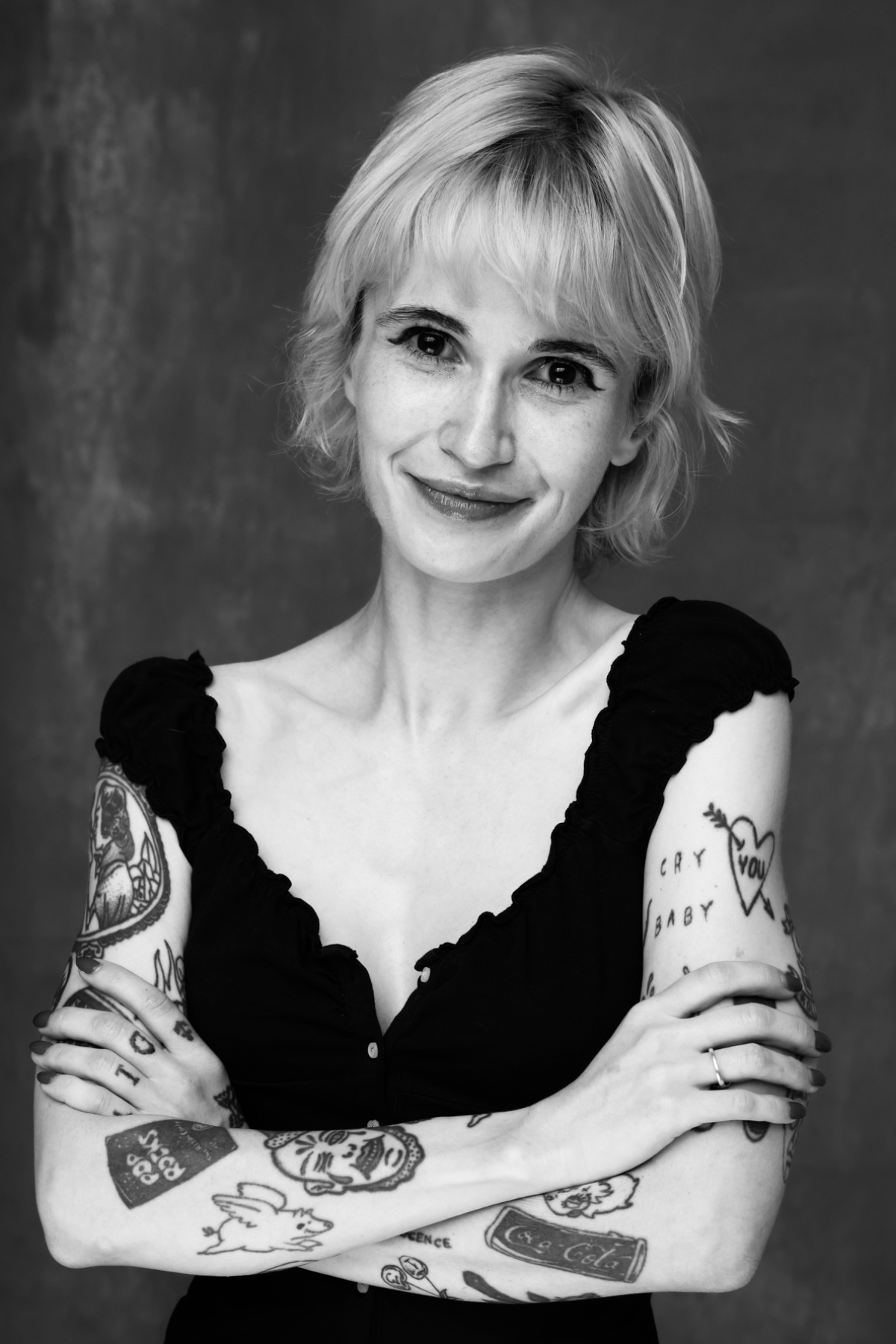 Taylor Drew smiling with her arms crossed, in black and white against a dark backdrop